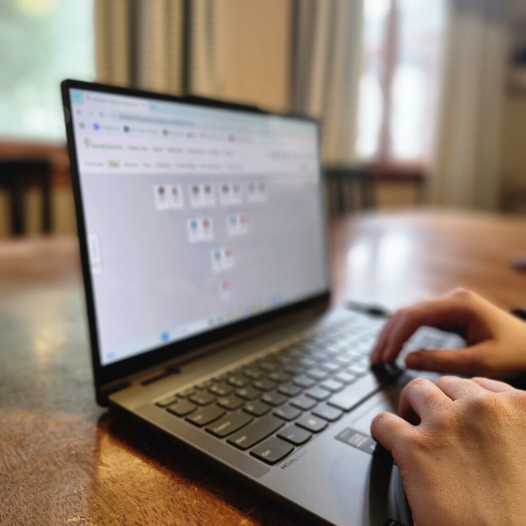 Open laptop on a table with two hands on the keyboard. The screen shows a family tree from a family history.