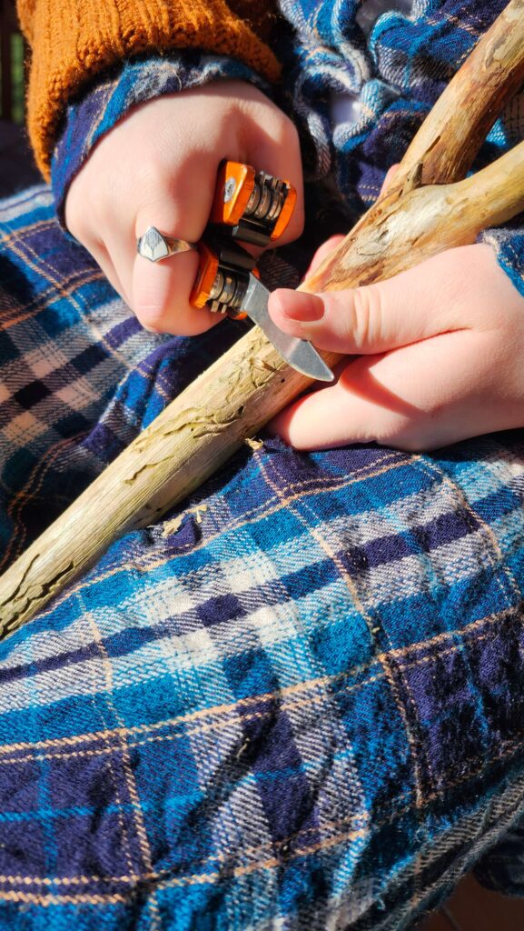 Hands whittling a stick with a pocket knife.