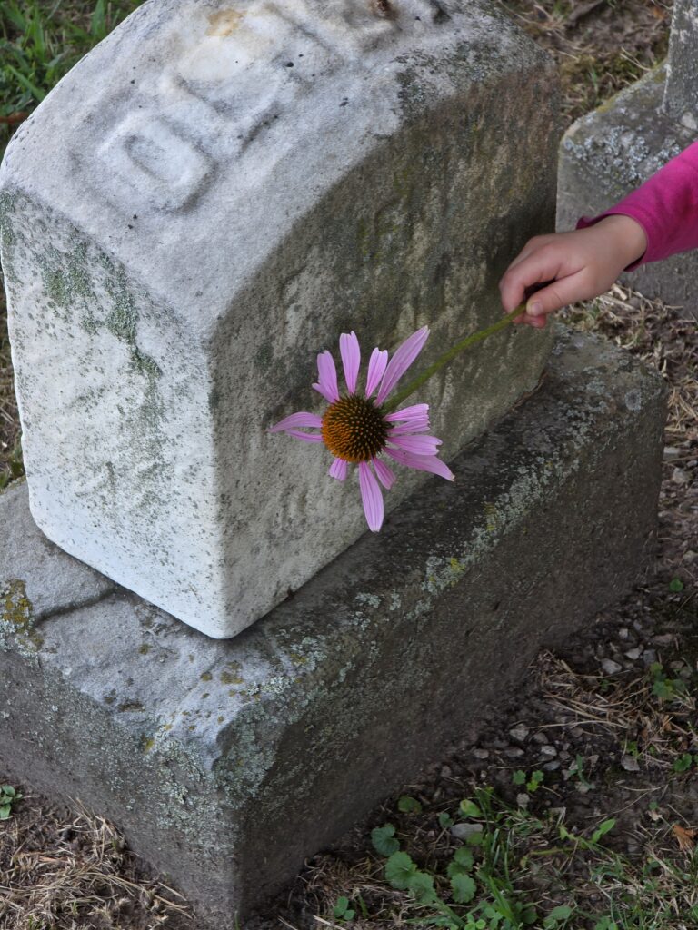 family cemetery visit headstone photo with hand placing a flower