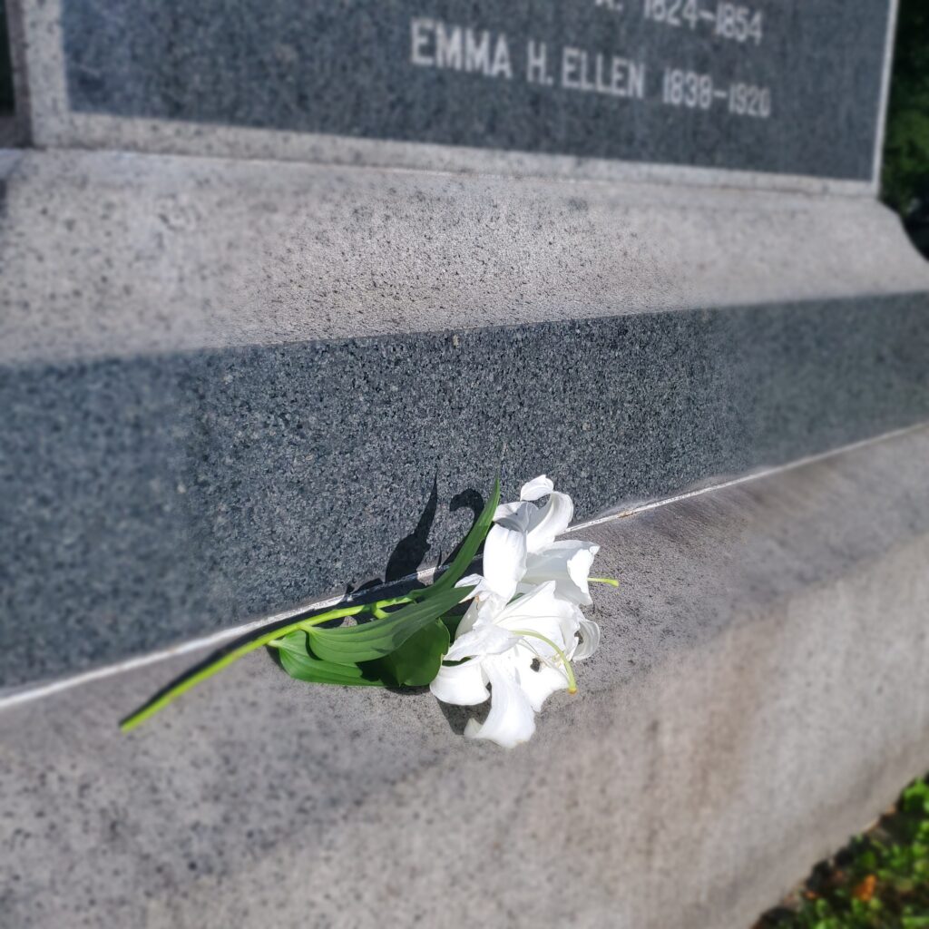 headstone with white day lilies at its base placed according to cemetery etiquette for families