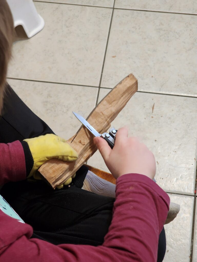 Child's hands carving a piece of wood over a tile floor.
