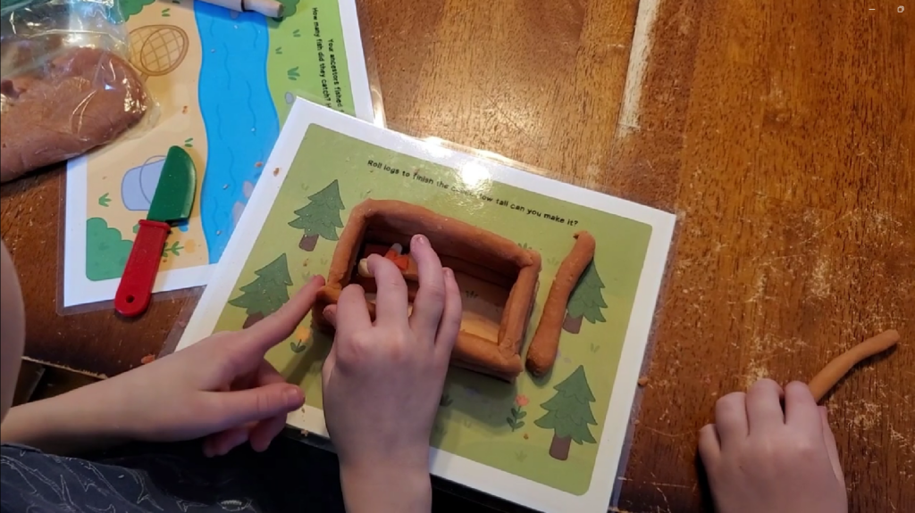 Children's hands molding playdough on laminated mat to learn hands-on family history on a wooden table.